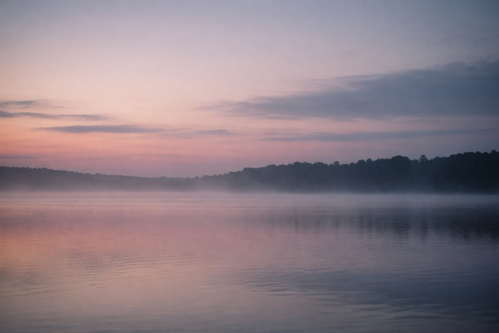 minimalist twilight horizon over still water, muted gray-blue tones, soft mist above lake, distant tree line fading into haze, low contrast lighting, emotional dusk atmosphere, calm reflective mood, cinematic negative space, no people, therapeutic aesthetic